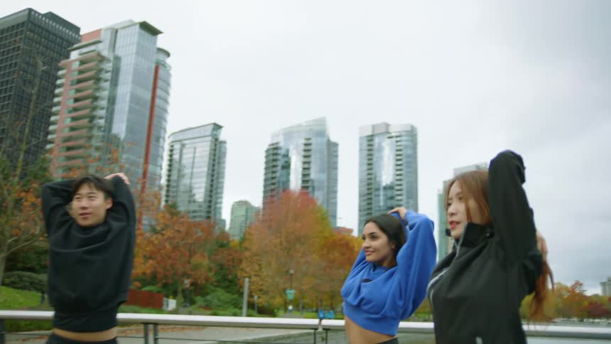 Group of young friends stretching on the park close to the lake next to the city
