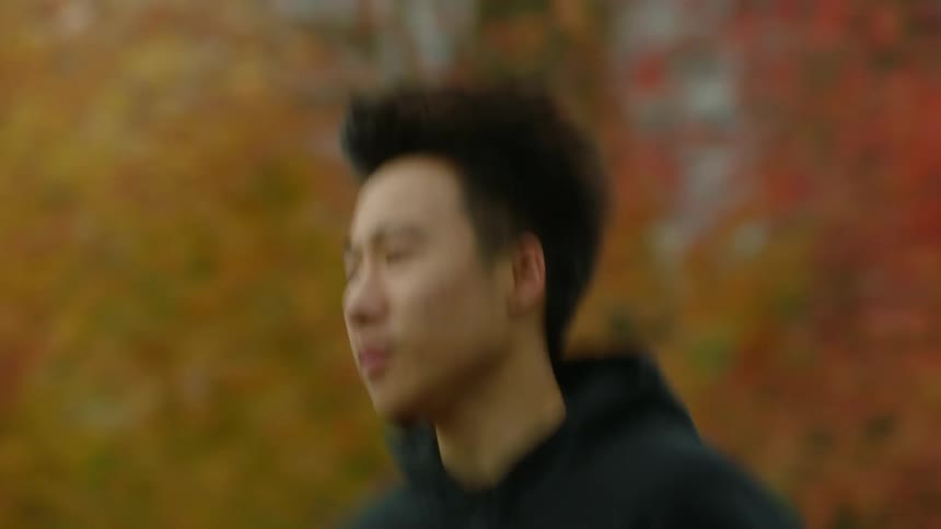 Man with black hoodie and man with black raincoat jog in city park with autumn trees