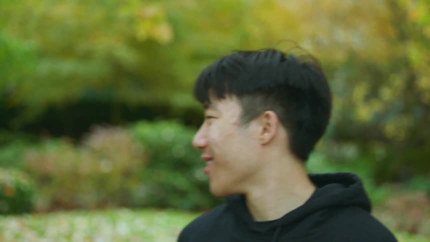 Man with black hoodie faces camera and shakes hands wit man with braids and black raincoat in public park