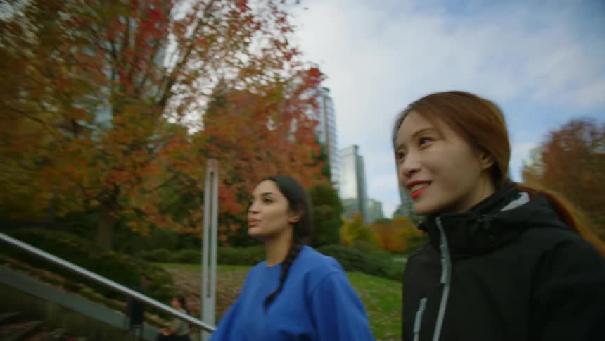 Woman with brown hair and woman wearing blue sweater jogs in public park going up stairs