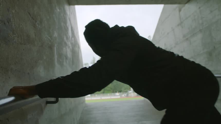 Young man wearing black clothes stretching on a concrete hallway near a running track