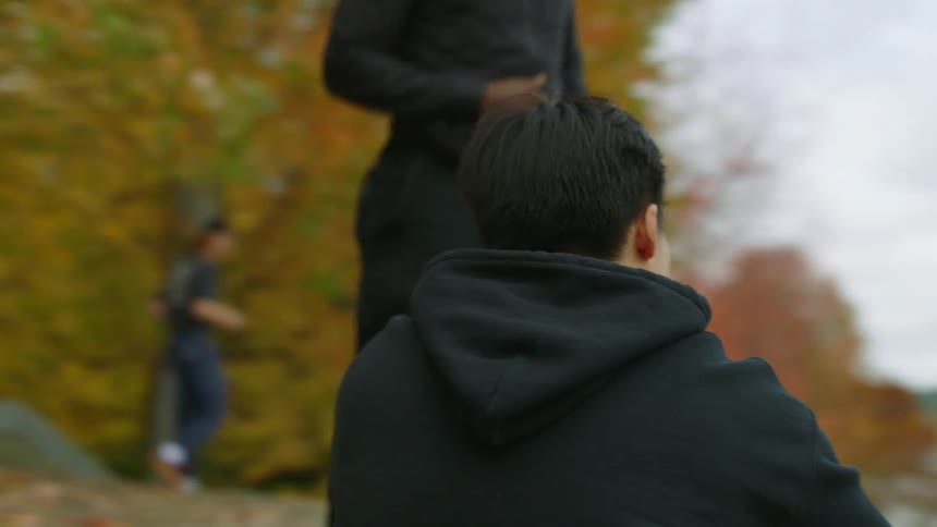 Man helps a tired friend to get up and start jogging on a park near a lake