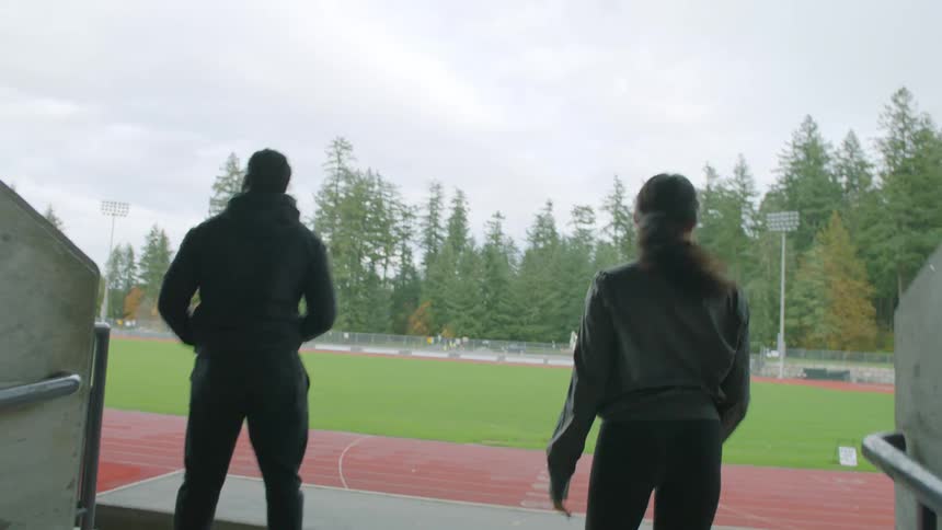 A man and woman high five as they jog to and reach the end of a tunnel at a stadium