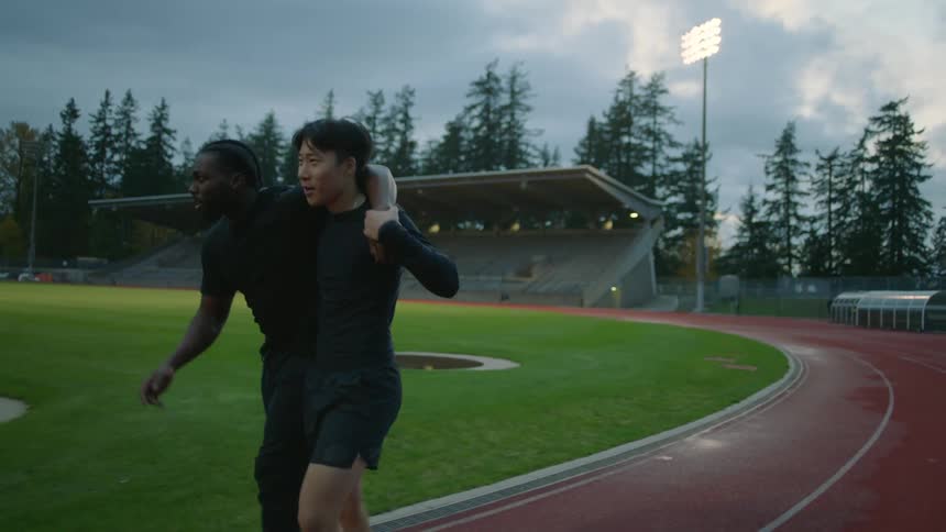 Coach helps an injured athlete on the running track at evening