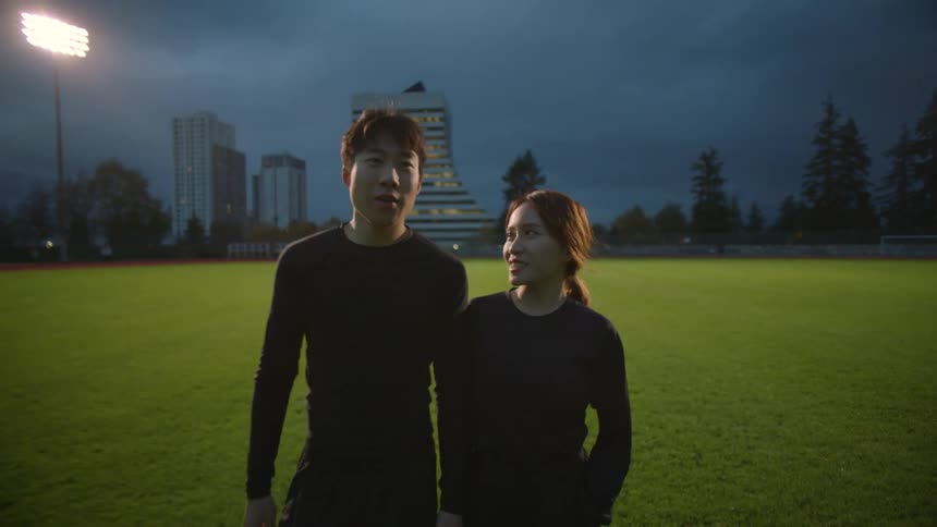 A man and woman high five and hug as they walk on the green grass of an empty stadium at night