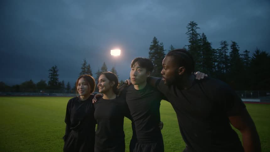 Four friends stand with their arms around each other on a soccer field