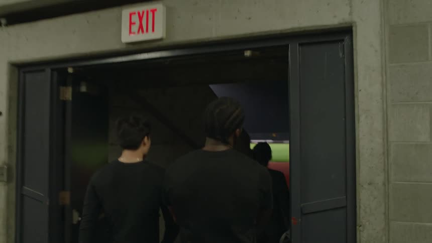 Group of friends walking down a hallway inside a stadium walk out a door to the field