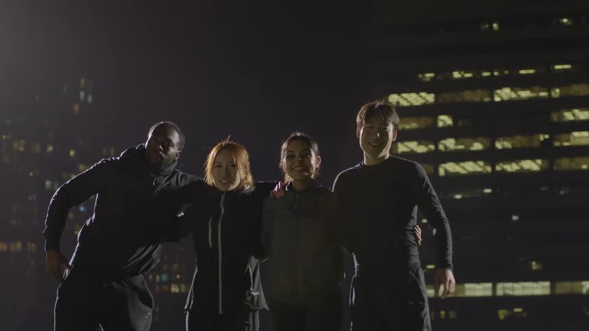 Group of friends hug each other looking at the camera in the city at night
