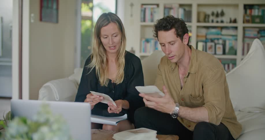 A man and a woman are sitting on a sofa and having a discussion about invitation envelopes in the daytime