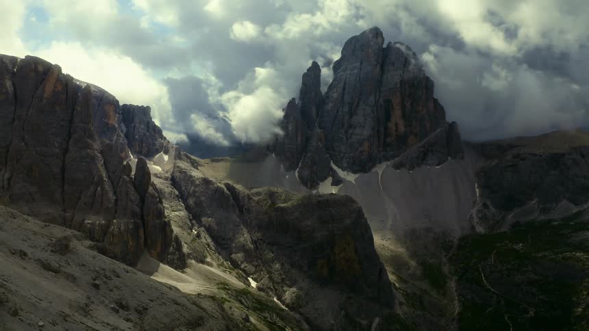 A rocky peak looms over a mountain range under a cloudy sky during the day