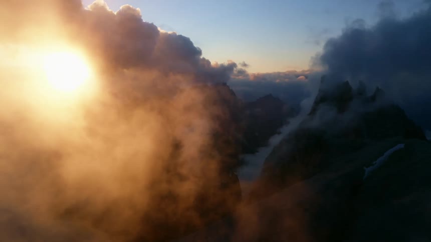The sun is shining brightly through the clouds with mountains in the distance