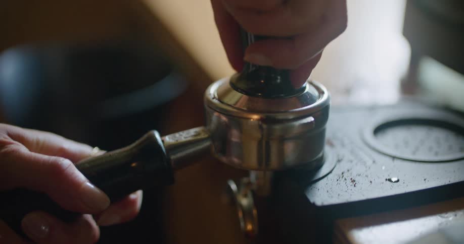 A hand presses down on the ground coffee in an espresso machine filter basket