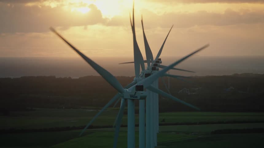 Turbines spinning on a wind farm as the sun shines through the clouds