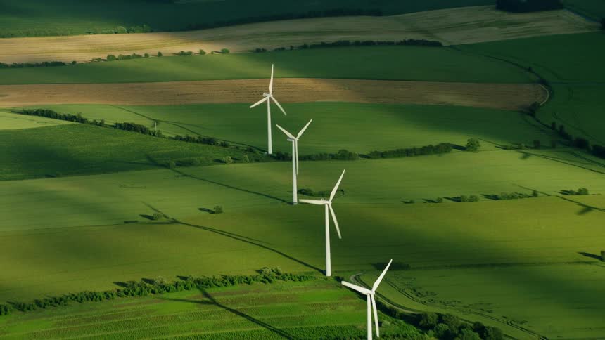 Turbines spinning on a wind farm as the sun shines upon them