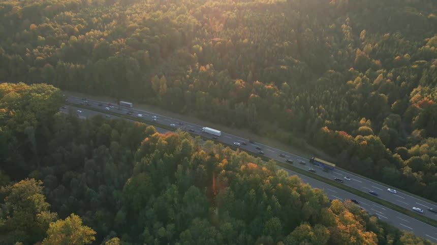 Sun glares from red tinted sky across highway cutting through trees some with fall foliage