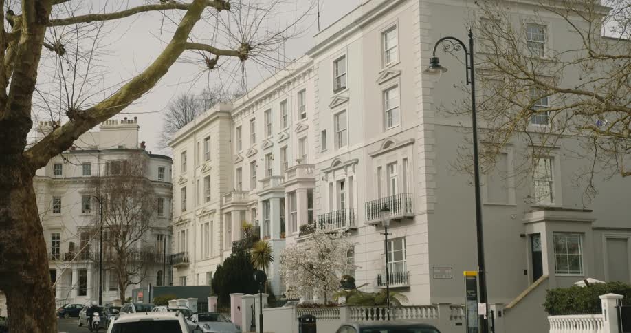 Car and motorcycle drive along road past apartment buildings under leafless trees