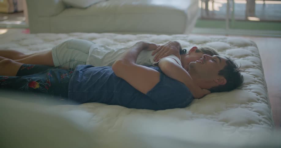 A man and woman embrace while lying on a bed during the day
