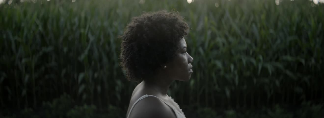 A woman standing outside near a cornfield lifts her head