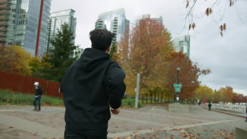 Young man wearing black jogging on the sidewalk next to the city