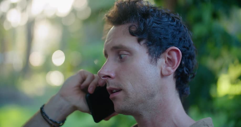 Man with bracelet talks on smartphone in green garden