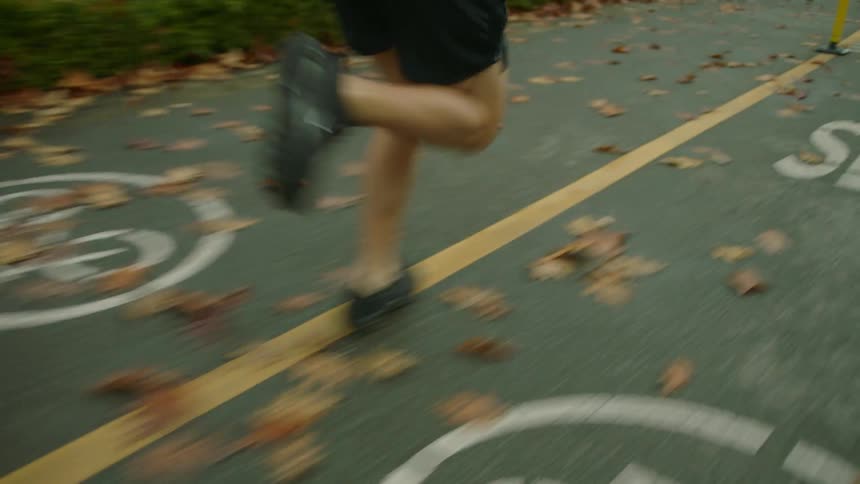 A man in sneakers jogging on a leaf covered road on a cloudy autumn day