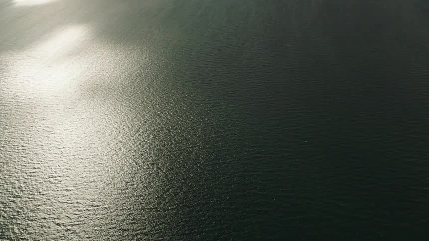 Aerial view of sun reflecting off sea water and small island