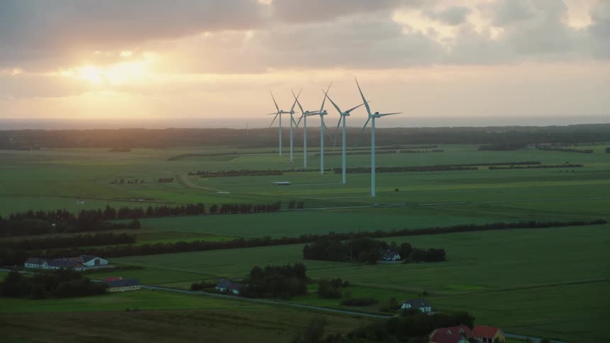 The farm land has a row of very tall windmills spinning in the morning