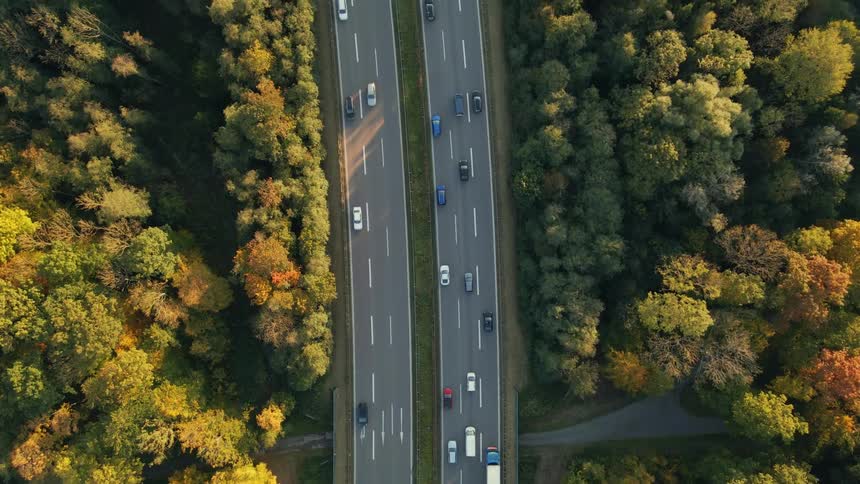 An aerial view of highway traffic traveling through a woodland area in the daytime