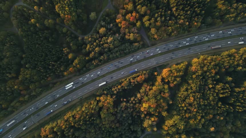 A birds eye view of cars driving on a freeway surrounded by autumn trees