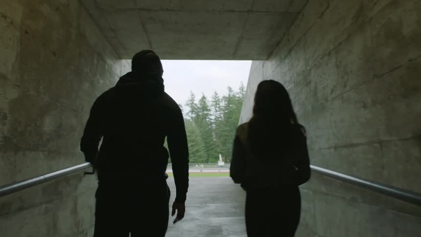 A man and woman walk through a tunnel towards a field