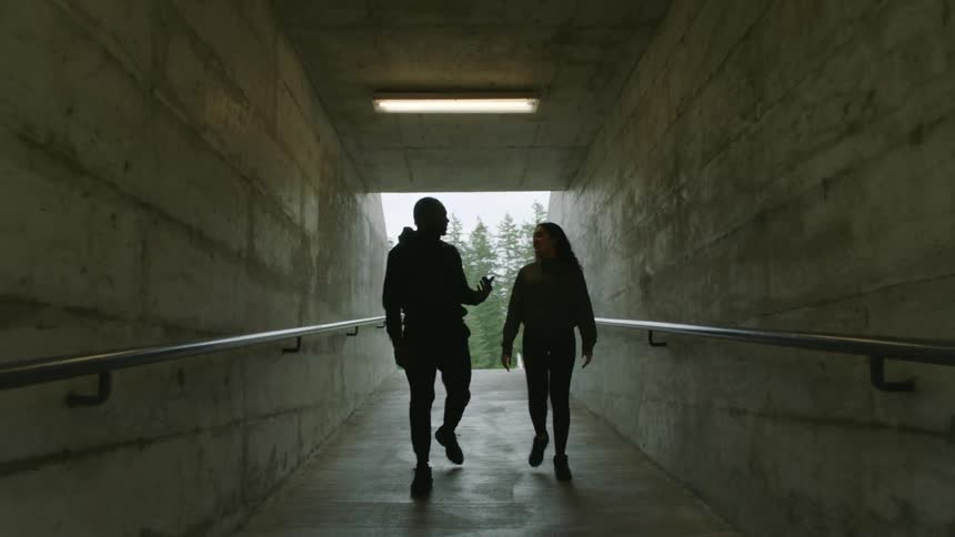 Man and woman walk along corridor talking with conifer forest in background