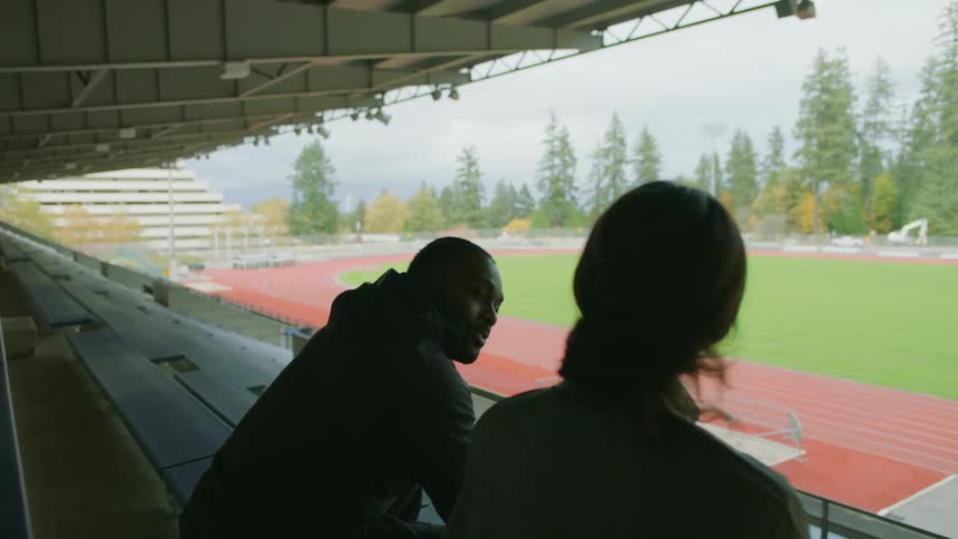 Two friends sitting on the stadium bleachers talking to each other