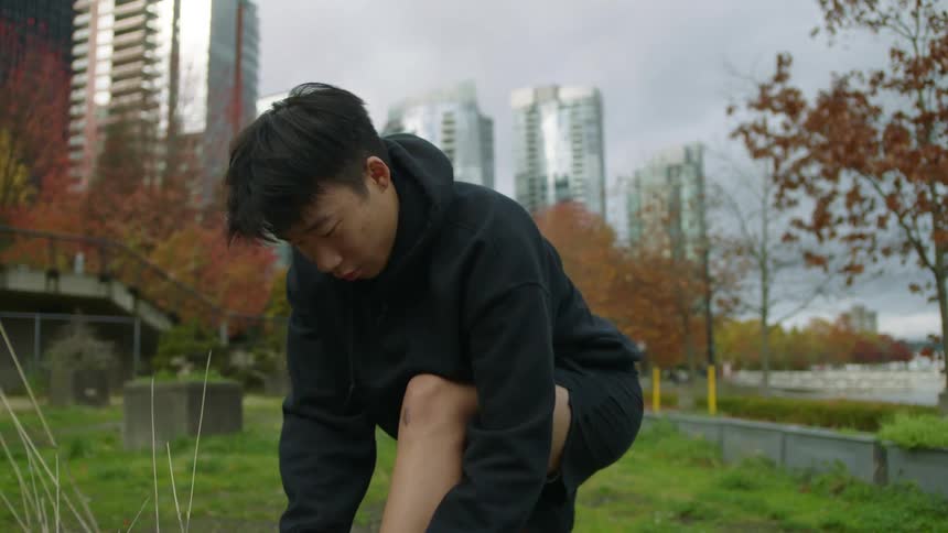 Man laces his sneakers in city park near downtown as bicyclist bikes by behind him