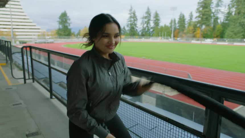 A woman exercises with battle ropes in the stands of an athletics field on a cloudy day