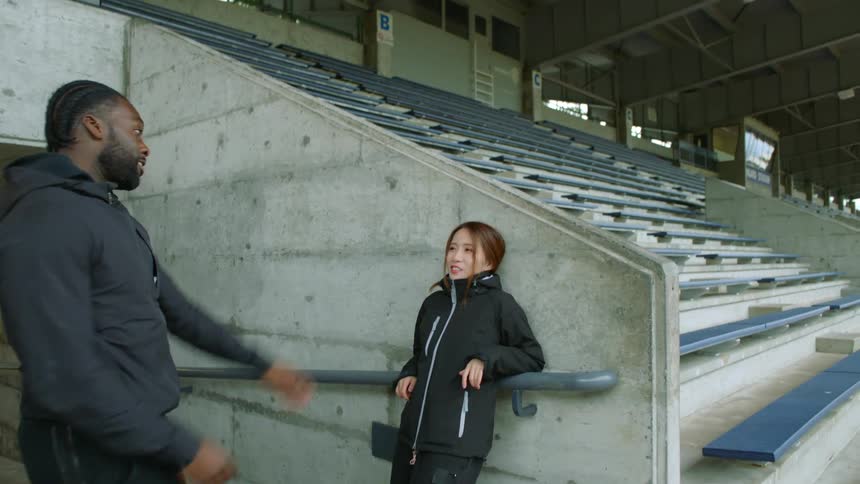 Woman resting near the bleachers in a stadium starts jogging with a friend