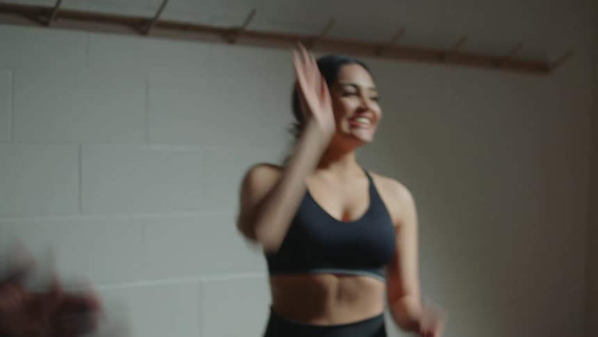 A group of people in athletic wear place their hands together before raising them in a cheer and clapping