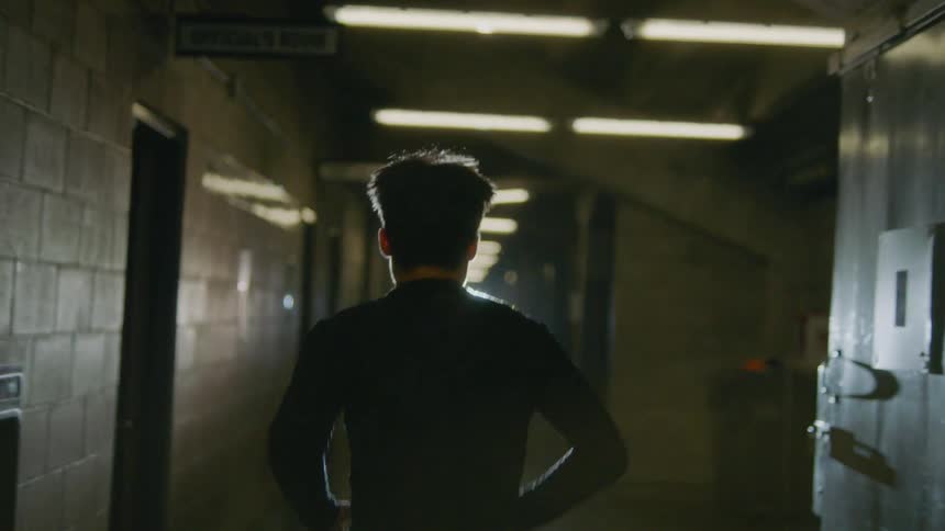 Silhouette of a man wearing black running inside a dimly lit hallway