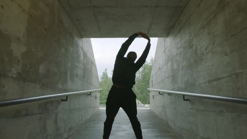 Young man wearing black sports clothes stretching on a stadium hallway