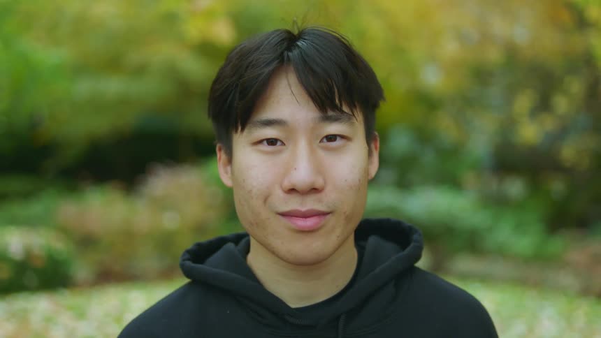 A young asian man smiles into the camera while standing outdoors during the day