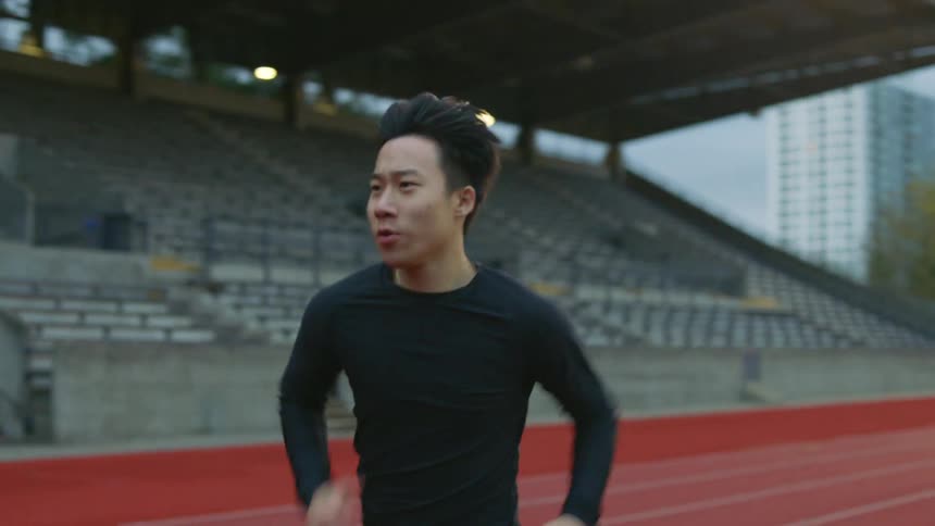 Two men run and train on an outdoor track at a stadium