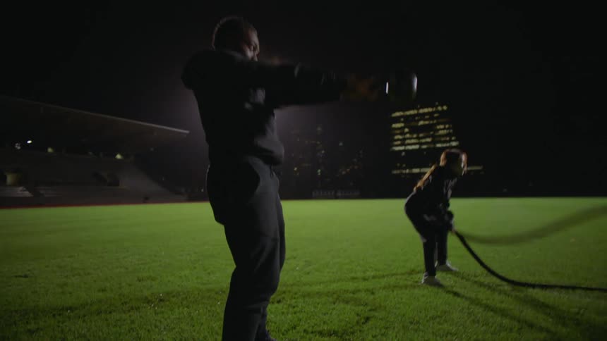 Two friends working out in a track field near the city at night