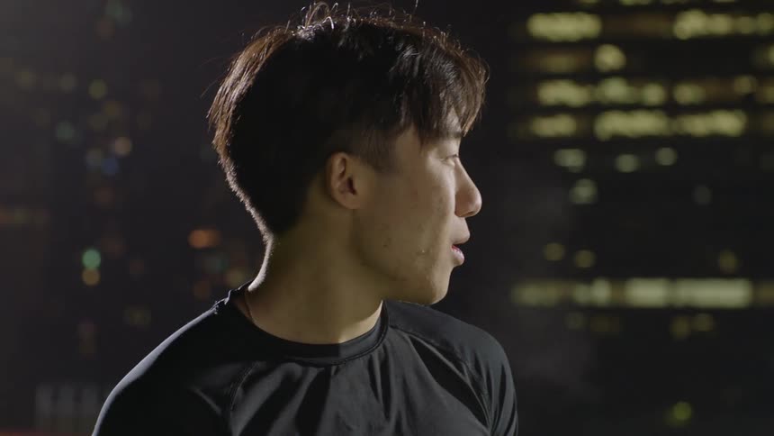 Young asian man smiles while looking at the camera next to the city at night