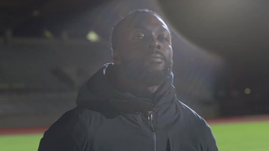 Young man wearing black jacket standing near a running track at night
