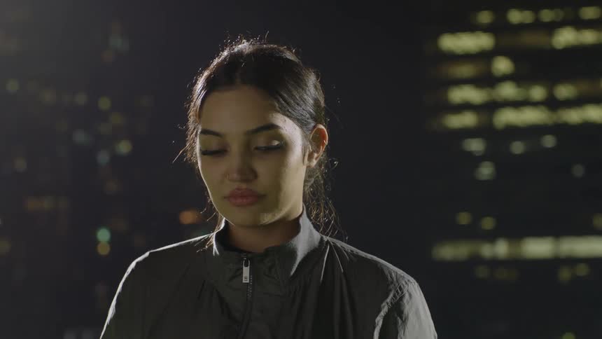 A young woman looks into the camera while standing outdoors at night