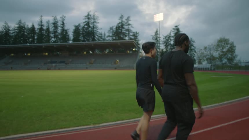 A pair of men talk while walking together along an outdoor running track on a cloudy day