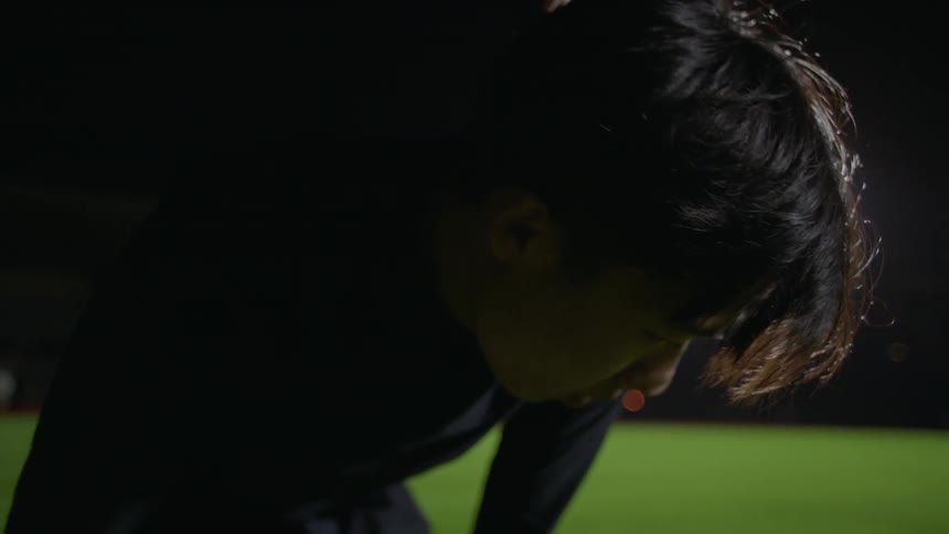 A young man on a field bends over and catches his breath as a woman comes and shakes his hand