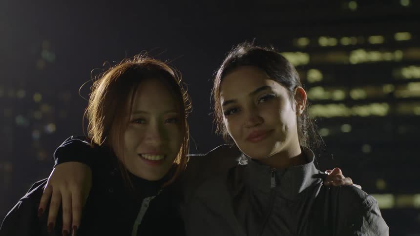 Couple of friends hugging and laughing in front of a building at night
