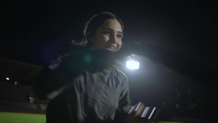 A woman training with ropes and high fiving a friend on an outdoor field at night