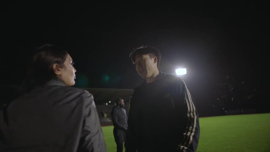 People are standing in an open field and a teenage boy and girl congratulate each other with a bright light shining in the distance