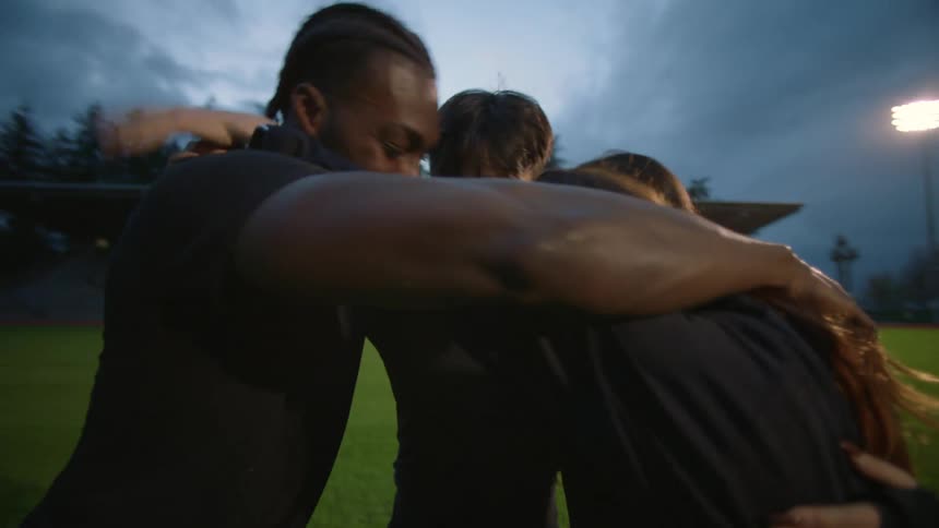 Group of friends wearing black clothes celebrate together on a stadium next to the city at night